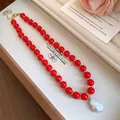 Detailed close-up of vibrant red acrylic beads and a large white baroque pearl pendant - Red
