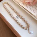 Close-up of beige acrylic beads and large baroque pearl pendant on a necklace - Brown