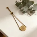 Close-up of a gold adjustable stainless steel bracelet with a religious coin pendant - Gold