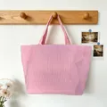 Detailed view of pink and white vertical striped canvas tote bag hanging on wooden rack - Red