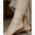 Detalle de una tobillera de trébol plateada en el tobillo de una mujer con vestido de tul - Plateado