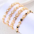 Gros plan de bracelets dorés avec motifs de cœur et fleur, ornés de perles blanches et noires - 16+5cm / Coeur Blanc