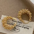 Detail shot of golden hollow flower basket hoop earrings with textured bead design - Ear Buckle / Gold