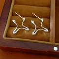 Detailed view of silver geometric wavy line stud earrings presented in a wooden jewelry box - Silver
