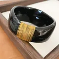 Macro view of marbled black resin bangle with elegant gold wire wrap detail texture - Black