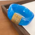 Detailed view of a blue marbled resin bangle featuring elegant gold wire wrap design - Blue