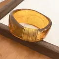 Close-up of a wide translucent amber resin bangle featuring an elegant gold wire-wrapped detail - Dark Coffee