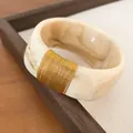 Macro detail of a wide marble resin bangle featuring a sophisticated gold wire wrapped section - Beige