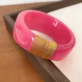 Detailed view of a wide pink resin bangle with elegant gold wire wrap detailing. - Rose Red