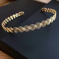 Vista dettagliata di un elegante bracciale rigido dorato ondulato su scatola nera - Oro