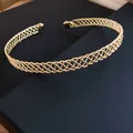 Vista ravvicinata di un elegante girocollo rigido in maglia dorata su scatola scura. - Oro