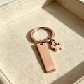 Vue détaillée d'un porte-clés en acier rose avec barre vierge et breloque patte d'animal. - Or rose