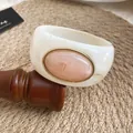 Gros plan d'un bracelet en acrylique blanc avec pierre ovale rose marbrée et bord doré - Ivoire-Rose