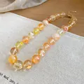 Close-up of ethnic acrylic beaded necklace with orange swirl pattern and gold chain. - Transparent Yellow