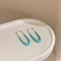 Dettaglio di orecchini geometrici in smalto blu chiaro su un vassoio bianco ovale - Fibbia per Orecchio a U / Base argentea / Blu