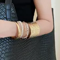 Gros plan détaillé d'un ensemble de joncs dorés et de bracelets en perles au poignet. - 59# Jonc - Blanc / Set de 5 pièces / Or