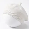 Close-up of a white knitted baby beret featuring soft textured yarn and top stem detail. - White