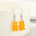 Primo piano di graziosi orecchini pendenti in resina a forma di orsetto arancione su una tazza - Arancione