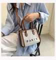 Vrouw zit en houdt canvas draagtas vast met PARIS-letters en bruine leren bies - Klein / Bruin