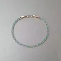 Vue de dessus détaillée d'un bracelet minimaliste en or rose avec des pierres baguette bleu clair - Style Carré Bleu Clair Entièrement Sertis de Strass / Or