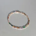 Nahaufnahme des eleganten Tennisarmbands mit regenbogenfarbenen Edelsteinen auf grau - Mehrfarbiger Quadratischer Vollstrass-Stil / Gold