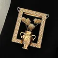 Close-up of golden frame brooch featuring a miniature vase and white dried flowers. - Hollow Photo Frame Brooch (3946) / Gold