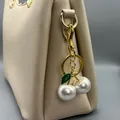 Macro view of elegant pearl cherry bag charm with green leaf on beige leather purse - White With Green Leaf