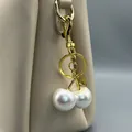 Detailansicht eines luxuriösen Perlen-Kirsch-Taschenanhängers an einer beigen Ledertasche. - Weiß