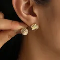 Eleganti orecchini a lobo in oro a forma di conchiglia, mostrati sull'orecchio della modella - Conchiglia Oro Texturizzata (6514201)