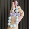 Detail shot of iridescent beaded phone charm with a purple bow and heart pendant - Purple
