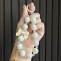 Detailed view of iridescent beaded keychain with a cream-colored resin bow charm - Off White