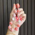 Close-up of a cute pink marbled beaded phone charm with a stylish red bow accessory - Red