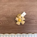 Nahaufnahme eines niedlichen gelben Stoffhaargummis mit Blumenmuster und weißem Etikett. - Gelb Blumig