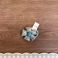 Detailansicht eines blauen Haargummis mit Stoffblumen auf einem Holzuntergrund. - Blaues Blumenmuster