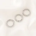 Vue détaillée de fermoirs à ressort argentés torsadés sur un fond en soie blanche. - Fermoir à Ressort Rond Torsadé (16mm) / 1 Pièce / Or blanc