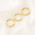 Gros plan de trois fermoirs ronds à ressort plaqués or 14K sur un tissu en soie blanche. - Boucle à Ressort Ronde (18mm) / 1 Pièce / Or 18K