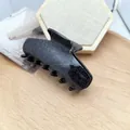 Detailed view of a black glitter cat-shaped hair claw clip resting on a wooden tray - Black Shimmer