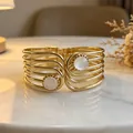 Close-up of a vintage-style gold multi-band cuff bracelet featuring round white stones. - Multi-layer Hollow Cat's Eye
