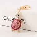 Elegante goudkleurige sleutelhanger met een roze strass schildpad op een wit blok - Coral Pink Glazed