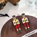 Festive enamel Nutcracker soldier earrings with pearl accents displayed on wooden plate - Red Yellow Black and White with Pearl (E32042-2)