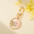 Close-up detail view of gold resin keychain with a real pink pressed flower insert - Pink Flower Green Leaf