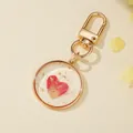 Close-up of a round resin keychain with a pink heart dried flower and gold flakes. - Heart Flower Petal