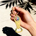 Décapsuleur porte-clés trophée Coupe du Monde 2026 doré tenu à la main au soleil - Style Amérique du Nord
