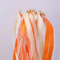 Close-up of colorful ribbon wands with golden bells and delicate lace for wedding party decor - Orange