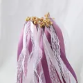 Close-up of purple and white ribbon wands with delicate lace and gold bells. - Purple