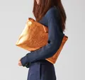 Detailansicht eines Modells mit einer glänzenden kupferfarbenen PU-Clutch-Umschlagtasche - Orange