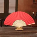 Traditional red folding paper fan with natural wooden ribs on decorative display stand - Red