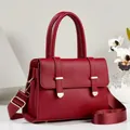 Detailed view of red pebbled leather handbag with gold hardware and wide shoulder strap - Red
