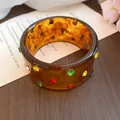 Nahaufnahme eines bernsteinfarbenen Acrylarmreifens mit bunten Strassverzierungen - #41 Silberstift - Braun - mehrfarbig - Strass-Stil