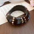 Dettaglio ravvicinato di un bracciale geometrico in acrilico nero con borchie dorate - Stile Arrotondato con Borchie Irregolari / Oro & Marrone